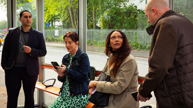 2 men and 2 women waiting at bus stop. 1 of the women looks uncomfortable with the conversation.